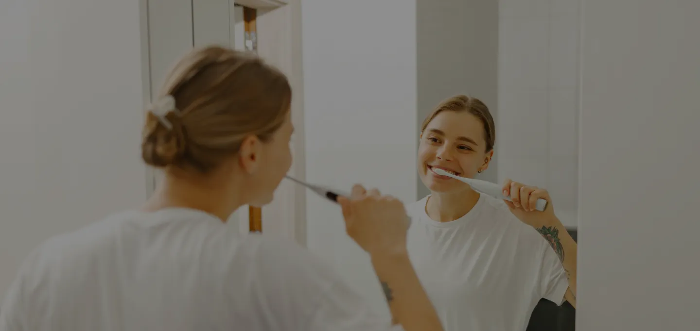 Woman brushing her teeth and smiling in the mirror